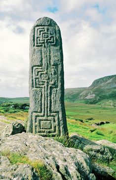 a large stone sculpture sitting on top of a grass covered field next to a lush green hillside