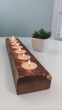 several lit candles sitting on top of a wooden block next to a potted plant