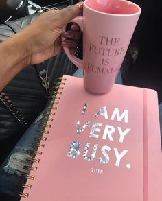 a person holding a pink coffee mug on top of a pink book with the words i am very busy written on it