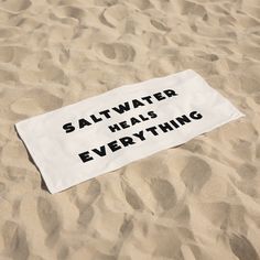 a white towel that says saltwater heals everything on it in the sand at the beach