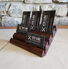 three business cards are placed in a wooden holder on a table next to a stone wall