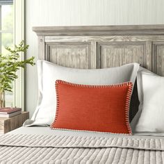 a bed with white and orange pillows in front of a wooden headboard next to a potted plant