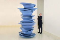 a woman standing next to a tall stack of blue plates in an art gallery,