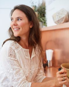 a woman in a white dress is smiling and holding a brown cup on the counter