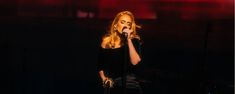 a woman singing into a microphone in front of a red light at a music concert