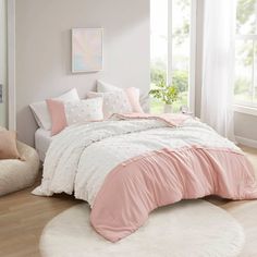 a bed with pink and white comforters in a room next to a window on a wooden floor