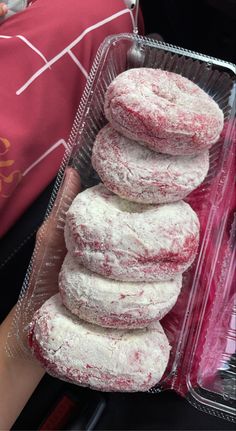 a person holding a plastic container filled with powdered donuts on top of each other