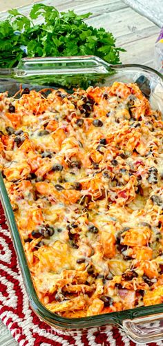 a glass casserole dish filled with lots of cheese and black olives next to cilantro