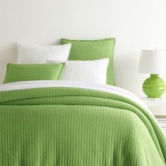 a bed with green bedspread and white pillows on top of it next to a lamp