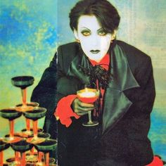 a man dressed in black holding a wine glass with candles on it and wearing red gloves