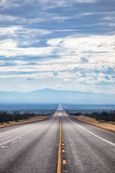 an empty highway stretches into the distance with mountains and blue sky in the back ground