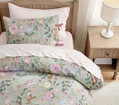 a bed with floral comforter and pillows on top of it in front of a night stand