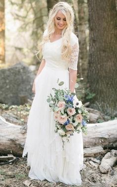 a woman in a white dress holding a bouquet and standing next to a fallen tree