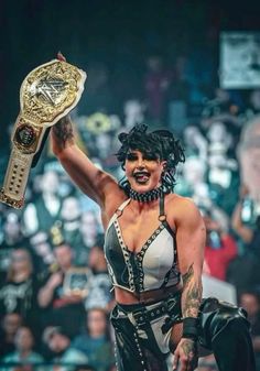 a woman holding up a wrestling belt in front of a crowd