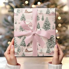 two hands holding a wrapped present in front of a christmas tree