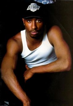 a man wearing a new york nets cap and white tank top sitting on a chair