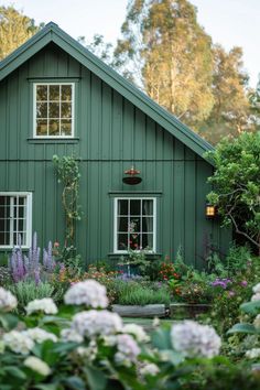 a green house with white windows and flowers in the foreground, surrounded by greenery