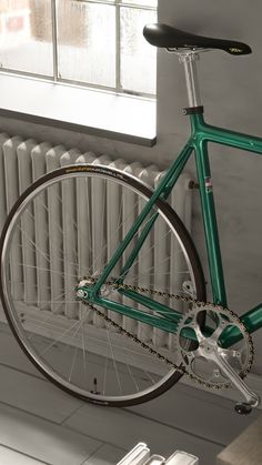 a green bike parked next to a radiator in front of a window on the floor