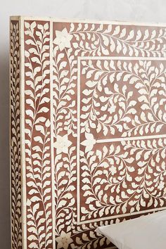 an intricately designed wooden headboard with white flowers and leaves on the top, in front of a gray wall