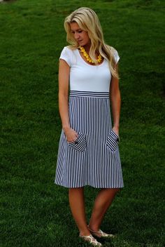 a woman standing in the grass wearing a white and black dress with stripes on it