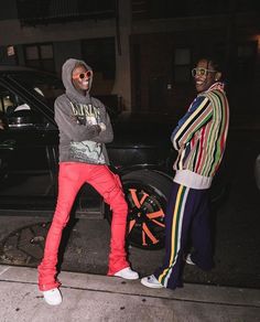 two men standing next to each other on the street at night with one wearing a hoodie