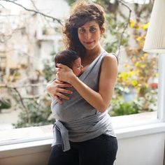 a woman holding a baby in her arms near a window with the sun coming through