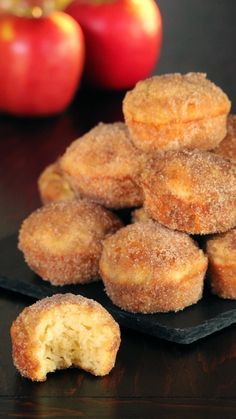 some sugared doughnuts on a black plate next to an apple and two red apples