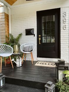 two white chairs sitting on top of a wooden porch next to a black front door