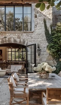 an outdoor dining area with wooden table, chairs and couches in front of a stone building