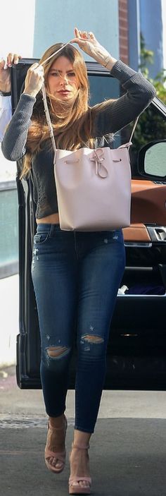 a woman in ripped jeans carrying a white purse and looking at the camera while standing next to a car