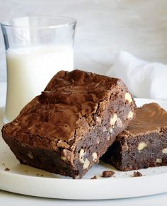 two pieces of chocolate brownie on a plate next to a glass of milk