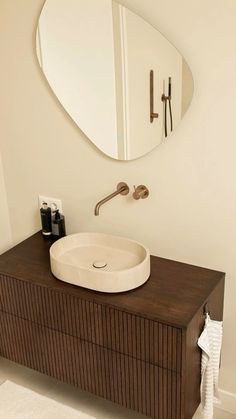 a bathroom sink sitting under a round mirror on top of a wooden cabinet next to a wall mounted faucet