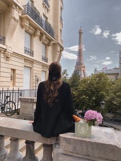 a woman sitting on a ledge looking at the eiffel tower