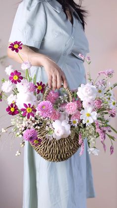 a woman in a blue dress holding a basket with pink and white flowers on it