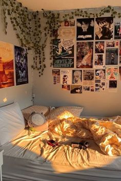 an unmade bed with lots of pictures on the wall above it and sunlight streaming through