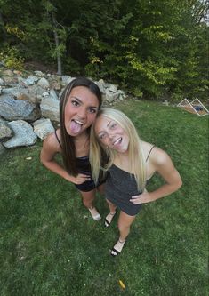 two young women standing next to each other in the grass