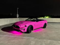 a pink car parked in a parking lot at night with its hood up and lights on