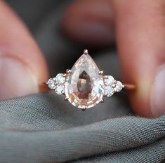 a close up of a person holding an engagement ring with a pear shaped morganite