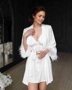 Make your bridal party feel luxurious and pampered with our White Feather Bride Robe Set! Each set includes delicate bridesmaid robes with a matching nightdress for the bride. The bride's nightgown and robe feature stunning feather sleeves for a touch of glamour. This elegant and stylish set makes the perfect bridesmaid gift to show your appreciation for your closest friends on your special day. Let your bridal party relax in style and comfort with this sophisticated White Feather Bride Robe Set Elegant Robe With Feather Trim For Wedding Night, Elegant Party Robe With Feather Trim, Feathered Robe For Wedding Night, Feathered Dresses For Wedding Night, Elegant Feather Trim Dress For Wedding Night, Elegant Wedding Robe With Feathers, Elegant Wedding Night Dress With Feather Trim, Wedding Satin Robe With Feathers, Wedding Satin Dress With Feather Trim