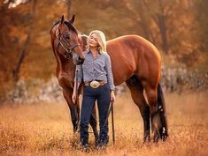 a beautiful blonde woman standing next to a brown horse in a field with tall grass