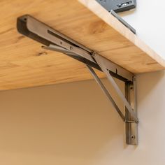 a wooden shelf with two metal brackets on it and a remote control in the background