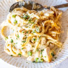 a white plate topped with pasta covered in chicken and sauce next to a spoon on top of a table