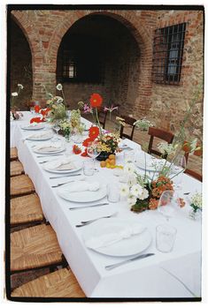 a long table is set with white plates and flowers