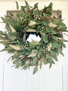 a wreath with white flowers and green leaves hangs on the front door's side