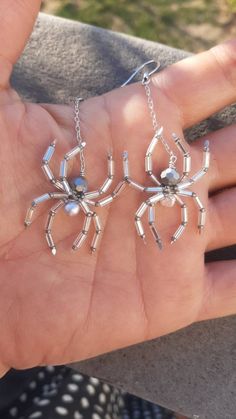 a person's hand is holding three silver spider pendants in their left hand