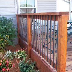 a wooden deck surrounded by flowers and plants on the side of a home's front porch