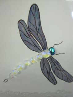 a glass dragonfly sitting on top of a white wall next to a blue beaded ball