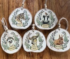 four ornaments with animals painted on them are sitting on a wooden table and hanging from twine strings