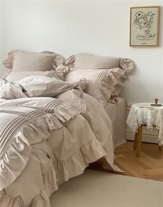 an unmade bed with ruffles on it in a white room next to a table