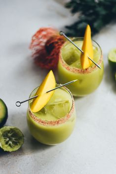 two glasses filled with green liquid and topped with fruit